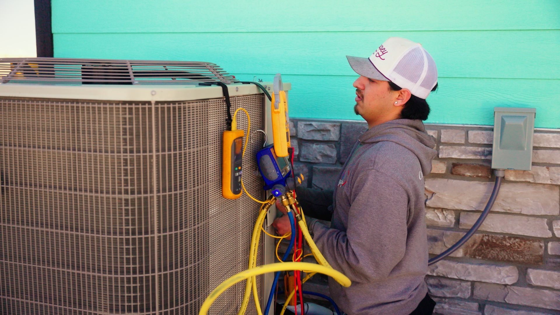 Technician using HVAC gauges on an outdoor air conditioner unit beside a house