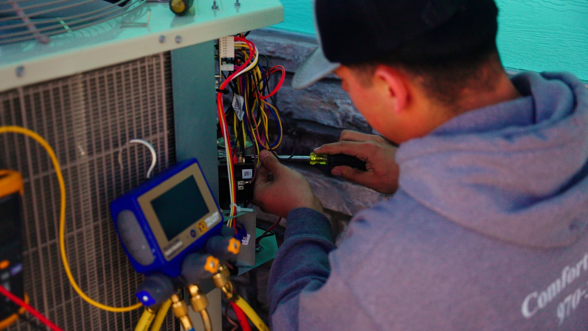 Technician inspecting wiring inside an electrical panel with a handheld meter beside a blue device