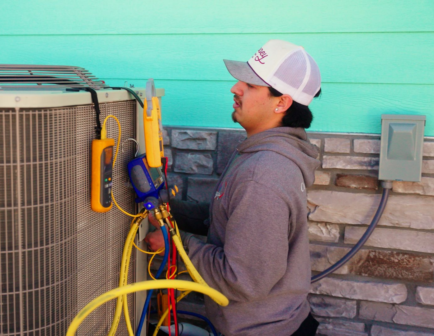 Technician inspecting HVAC unit outdoors with hoses and tools attached to the side