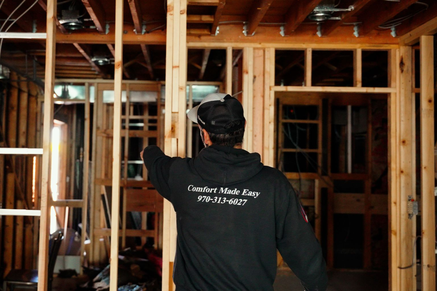 Person in a black shirt inspecting unfinished wooden house framing indoors