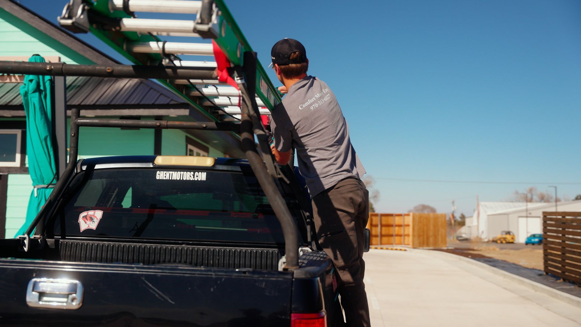 Person loading a green ladder onto a black truck in an outdoor parking lot