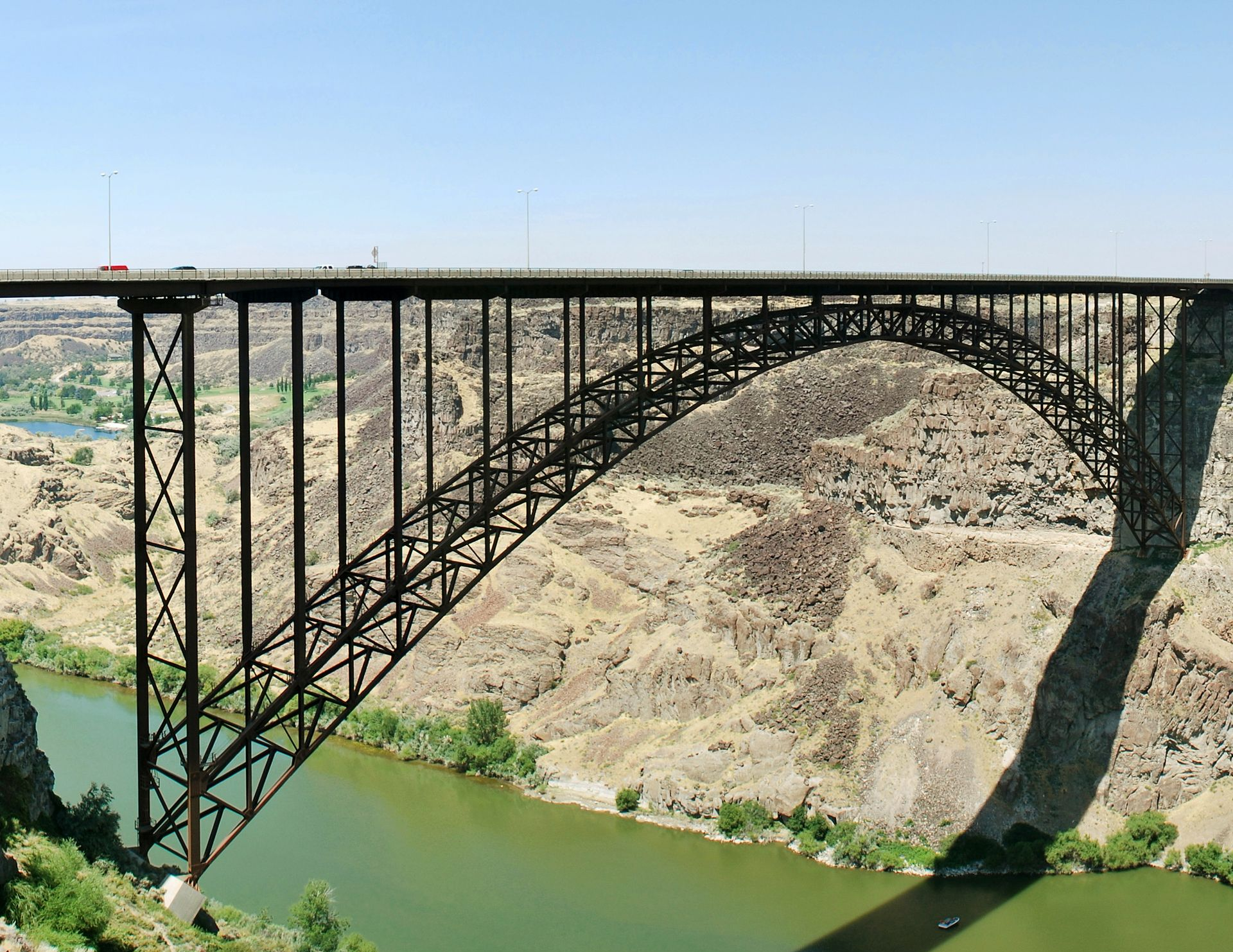 Steel arch bridge spanning a rocky canyon over green water under a clear sky