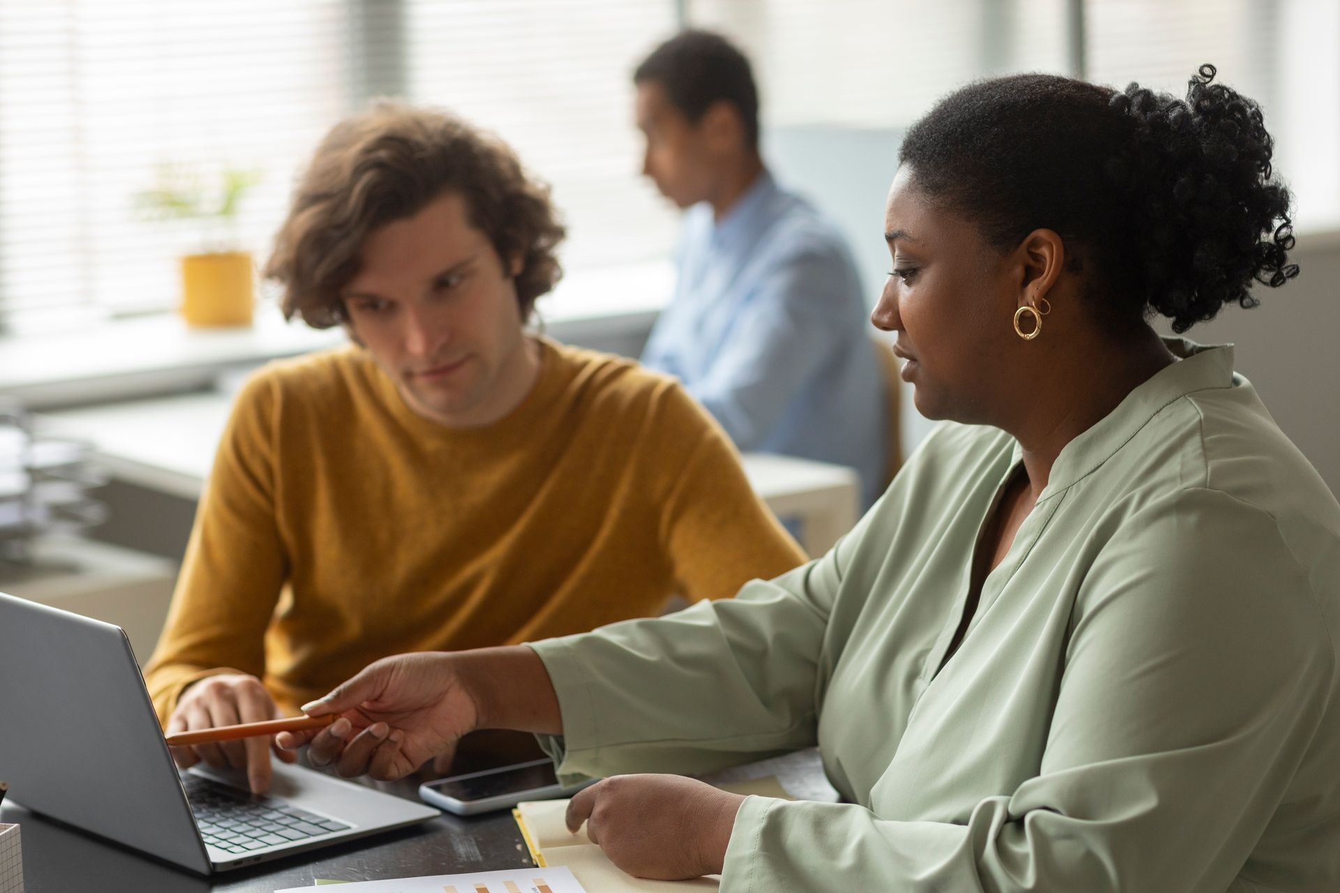 Two coworkers in a meeting reviewing documents beside a laptop and coffee cup.