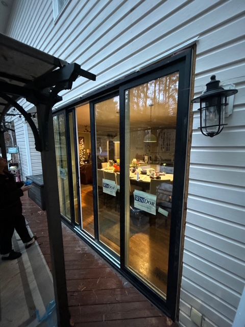 Black-framed sliding glass doors on a house. The interior, lit with warm light, is visible.