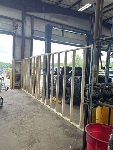 Interior view of a garage with a wooden wall under construction. A car lift and other equipment are also visible.