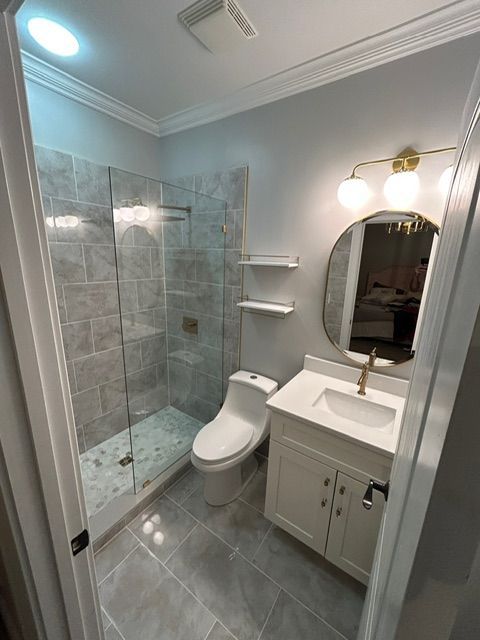 Bathroom with tiled shower, toilet, white vanity, round mirror, and gold fixtures.