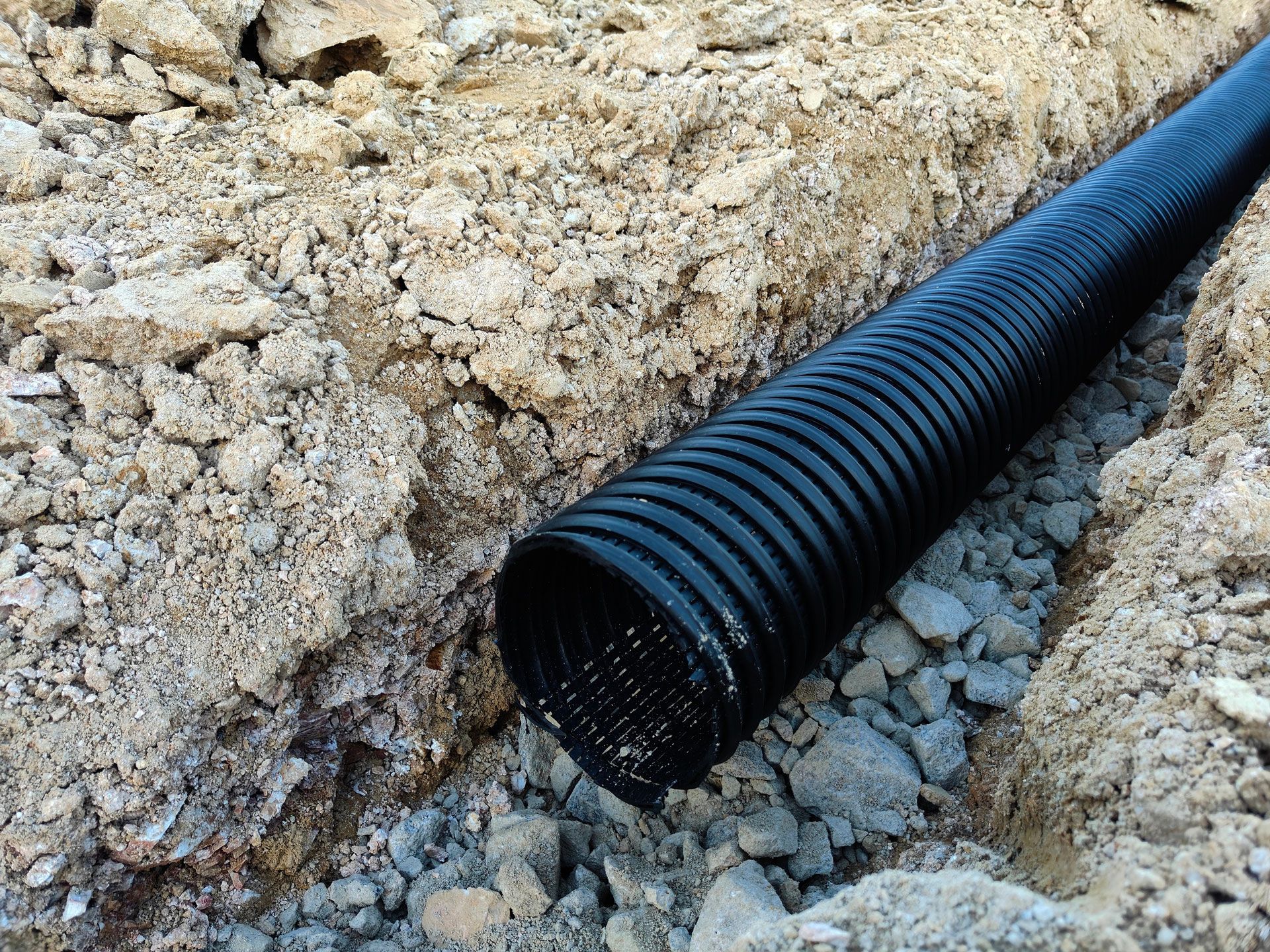 Black corrugated pipe installed in a trench dug in brown soil and rocks.