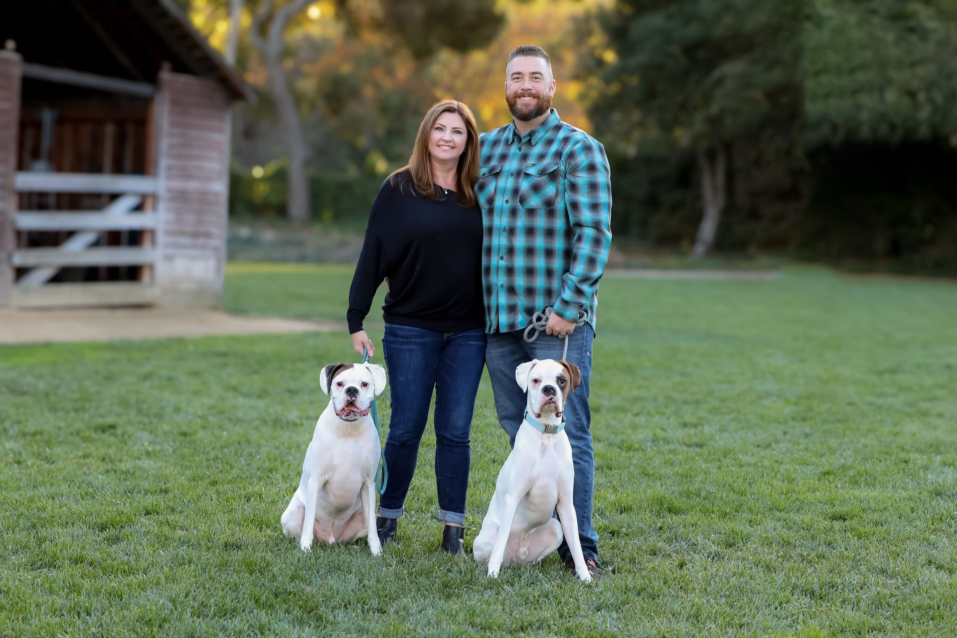 Couple standing on grass with two white dogs in front of a barn-like building