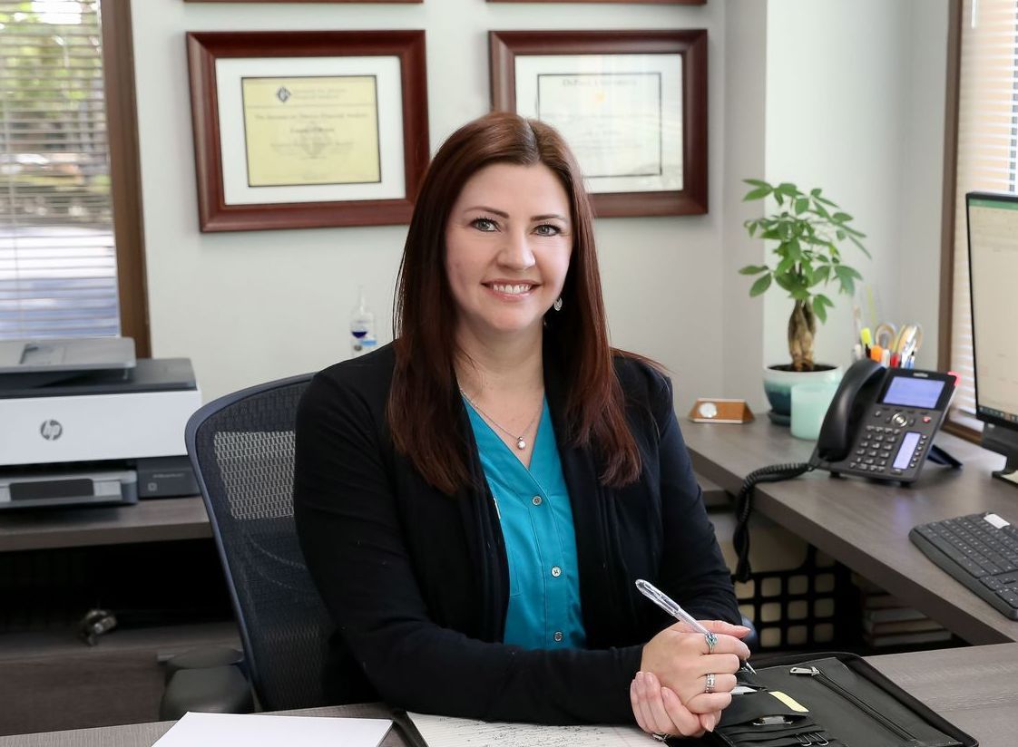 Woman seated at an office desk, smiling and holding a pen in a professional workspace.