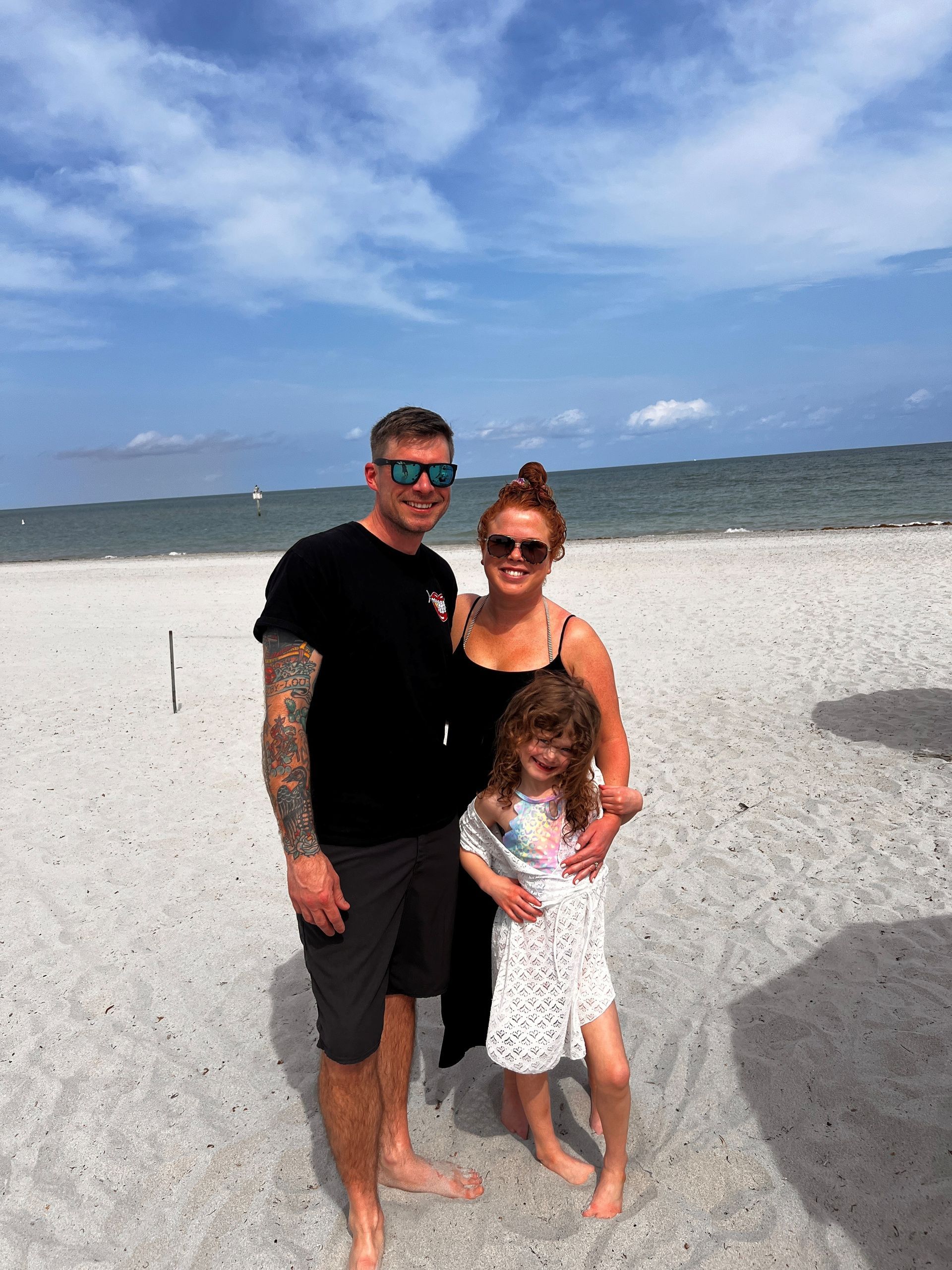 Three people posing on a sunny beach with white sand and blue water behind them