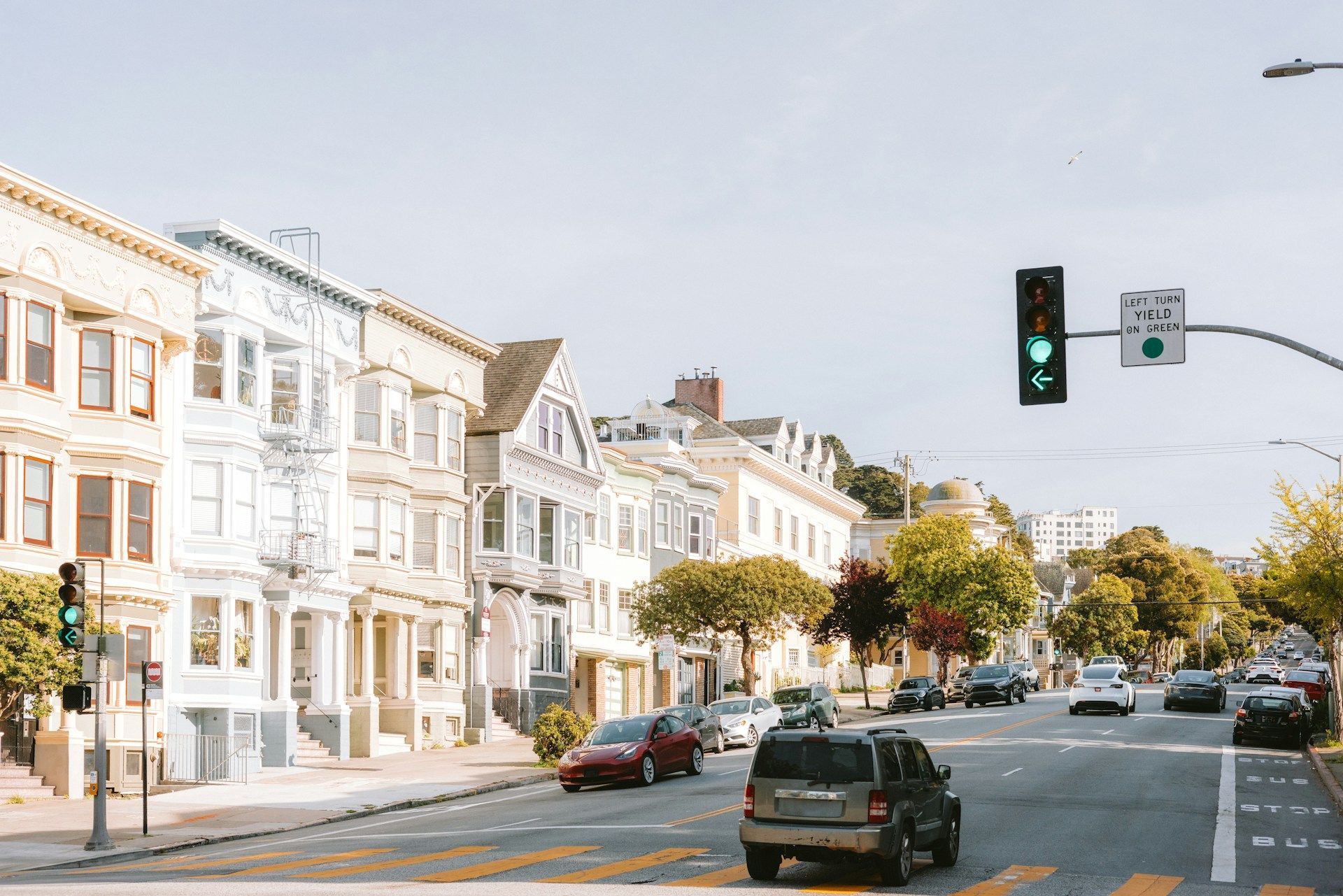Sunny city street with row houses, parked cars, and a green traffic light at an intersection