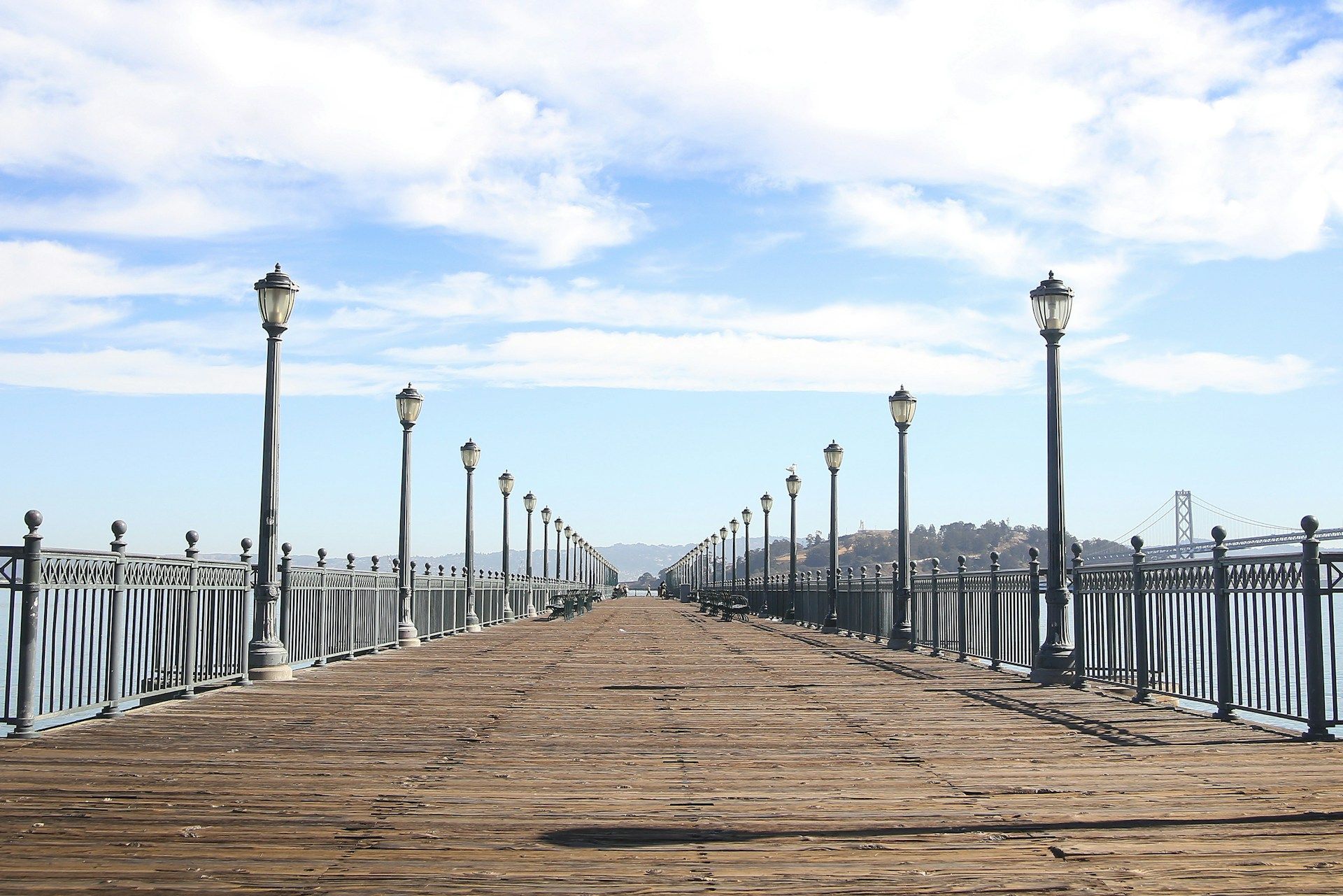 Stone pier with lampposts leading toward the horizon under a blue sky and clouds