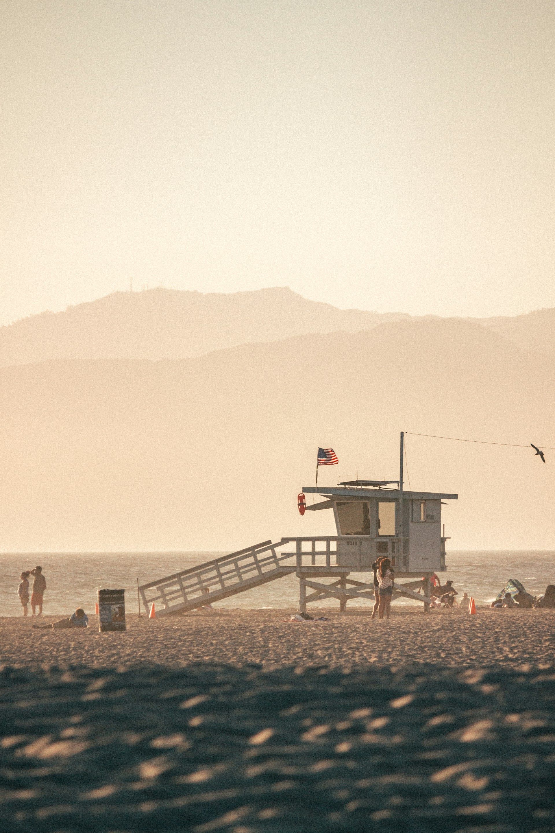 Lifeguard tower on a beach at sunset with hazy mountains in the distance and a small flag flying.