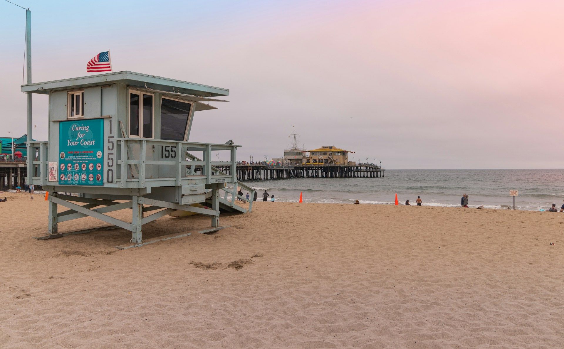Beach lifeguard tower on a sandy shore at dusk, with an American flag and calm ocean waves.