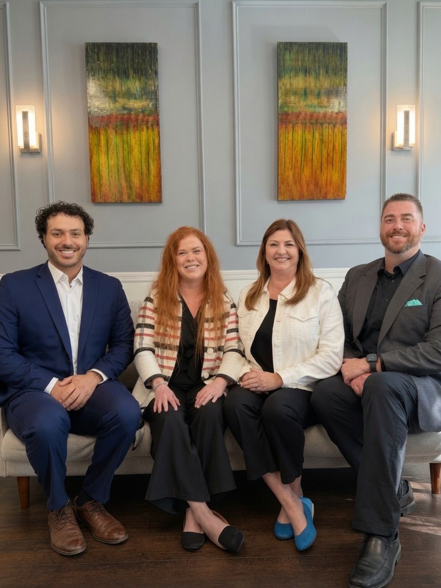 Four adults seated on a couch in a modern office, smiling beneath colorful wall art.
