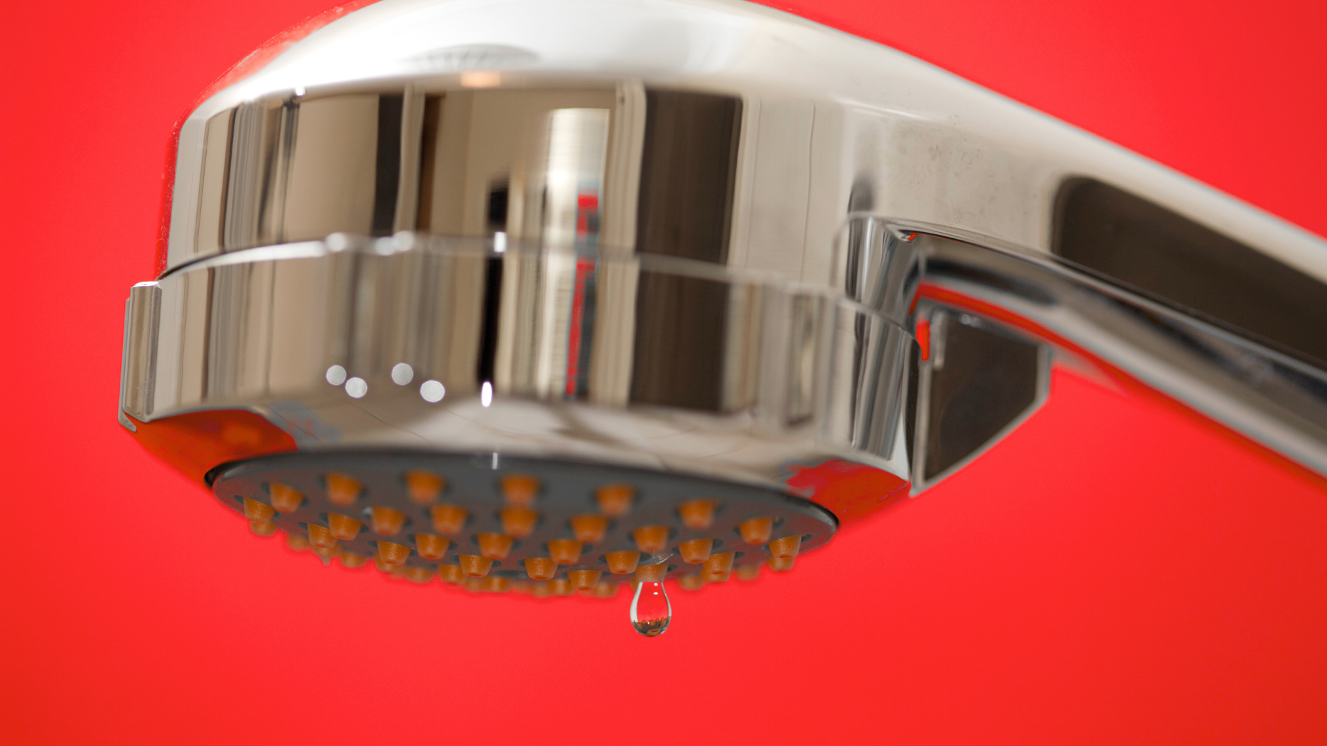 A close up of a shower head with a drop of water coming out of it.