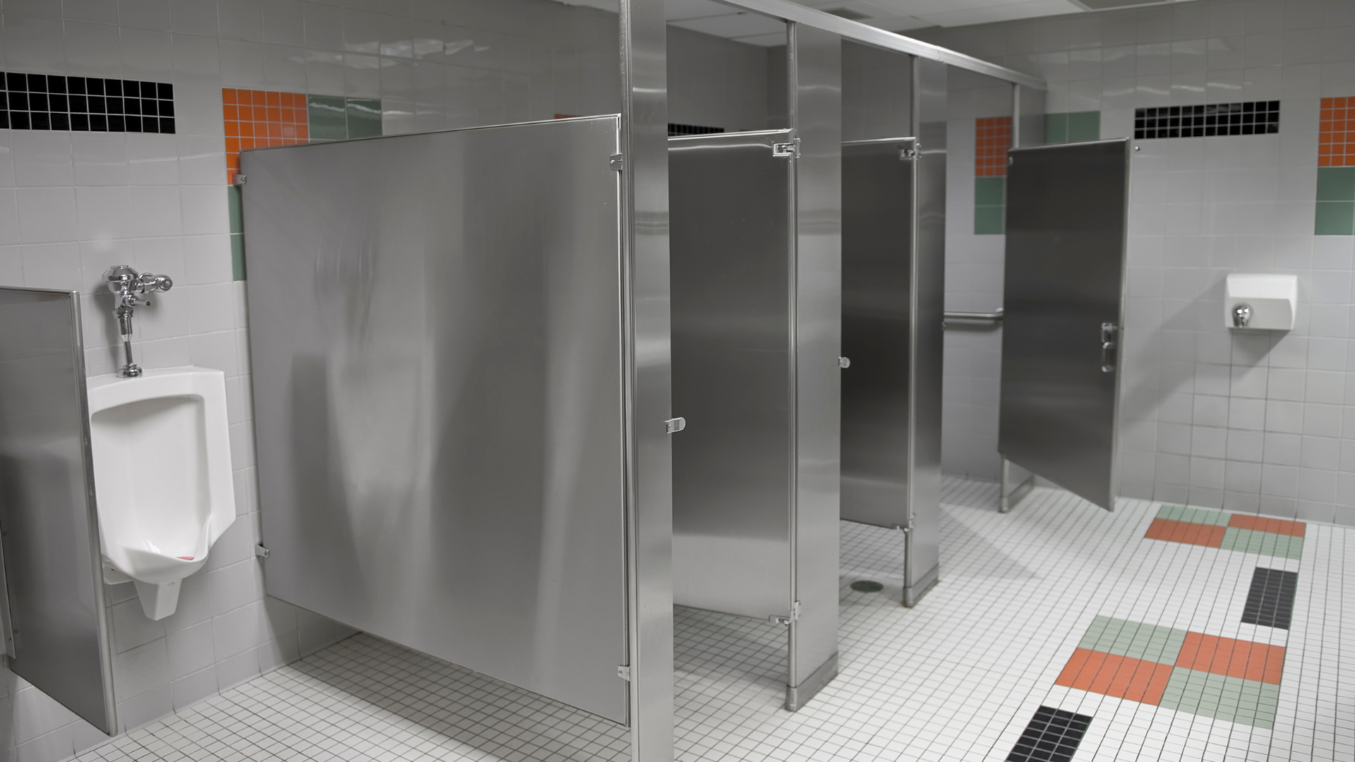 A public restroom with stainless steel stalls and a urinal