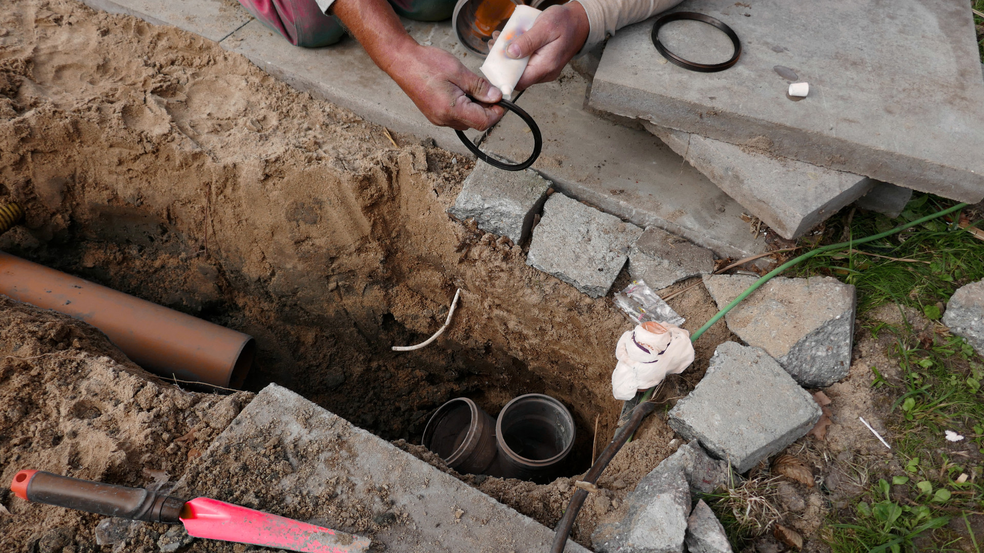 A man is working on a pipe in the dirt.