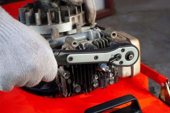 Close-up of a gloved hand repairing a small engine on an orange machine