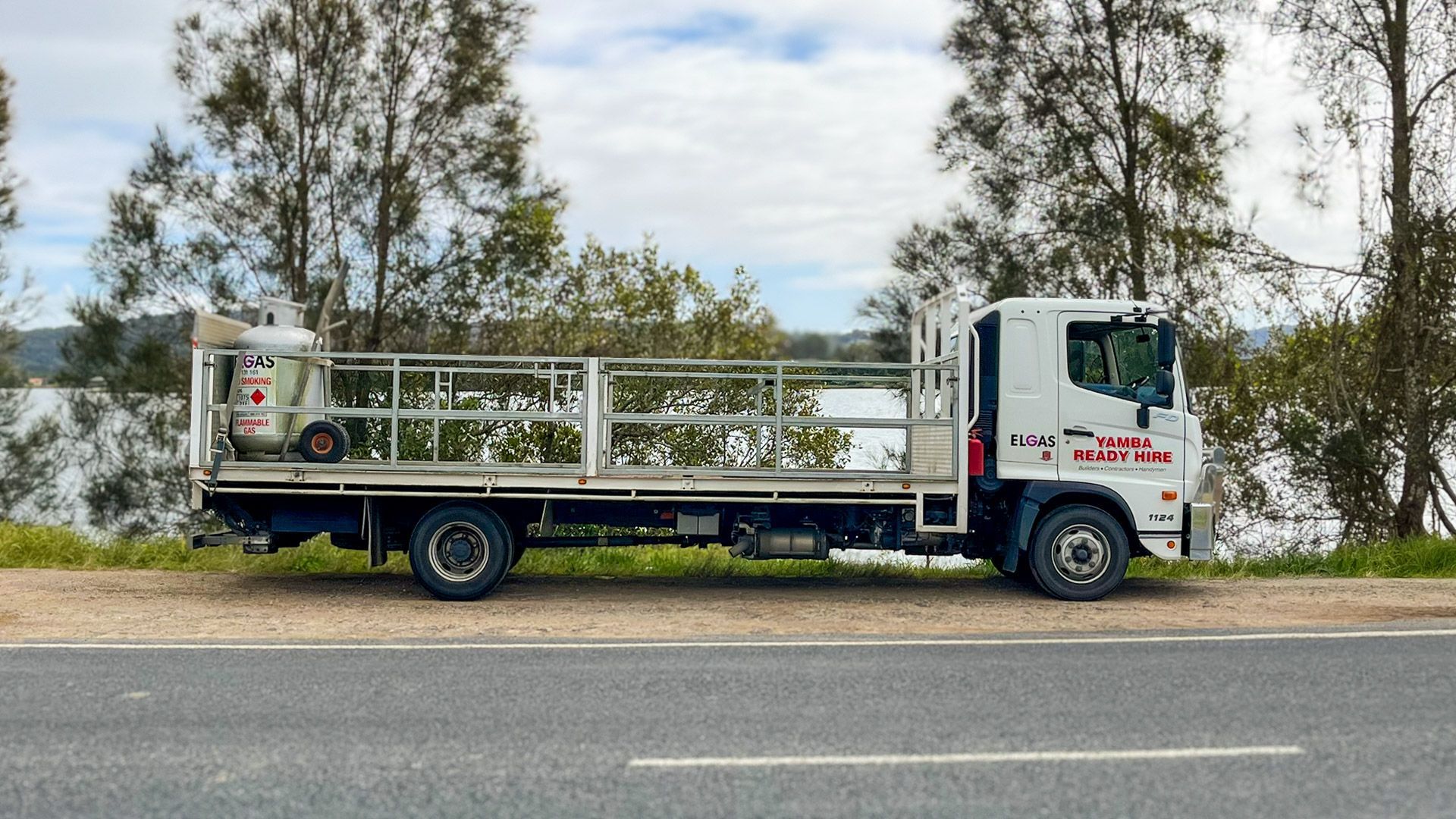 White flatbed truck parked beside a road with trees and cloudy sky in the background