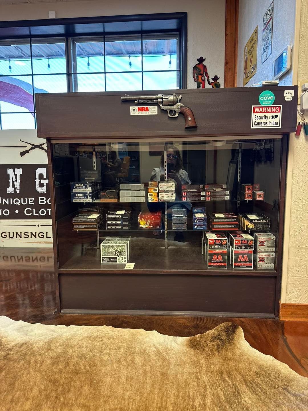 A gun store display case filled with ammunition. A revolver sits atop. Brown wooden exterior.