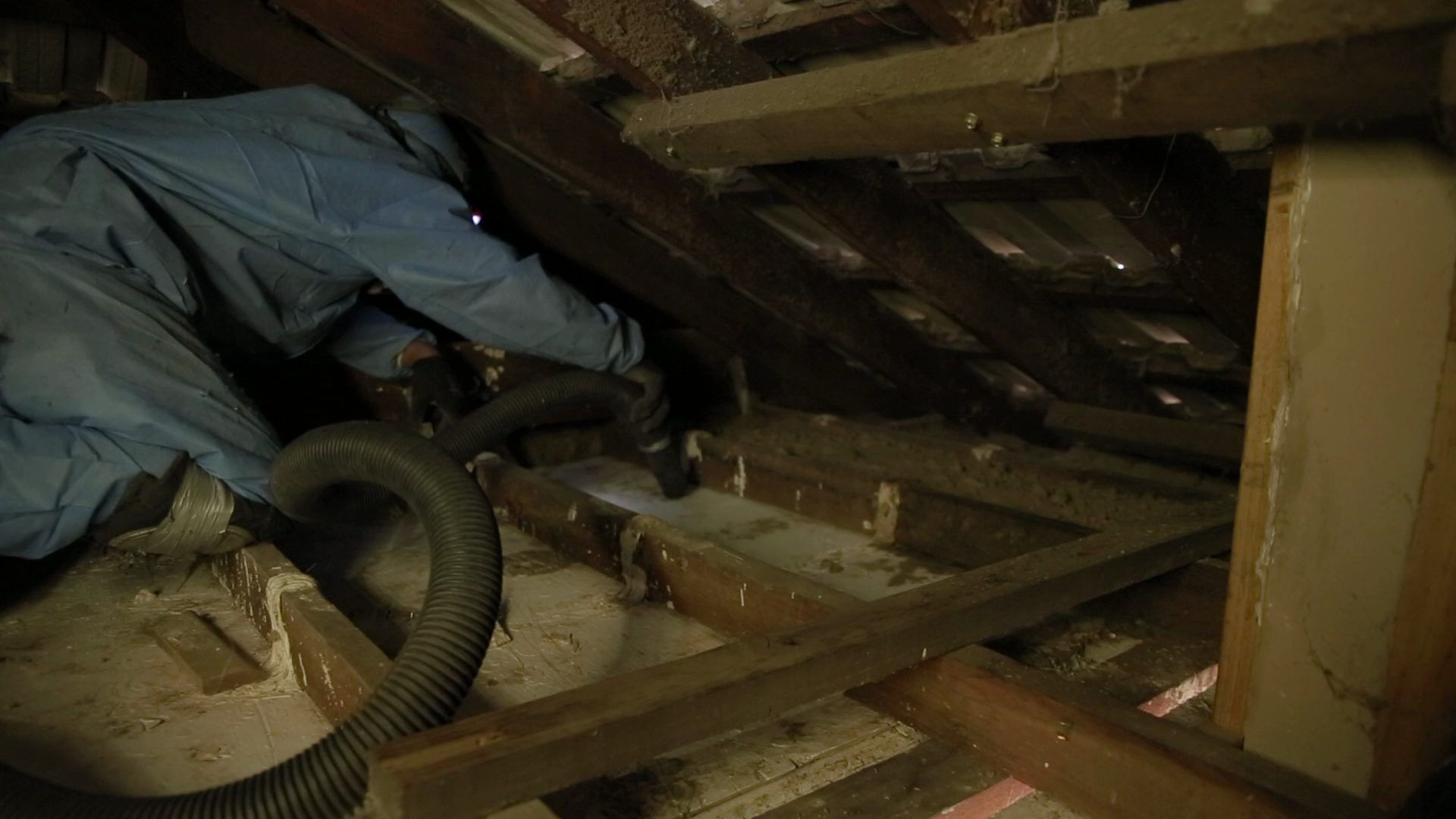 HEPA-filtered vacuum hose extracting dust from a roof cavity