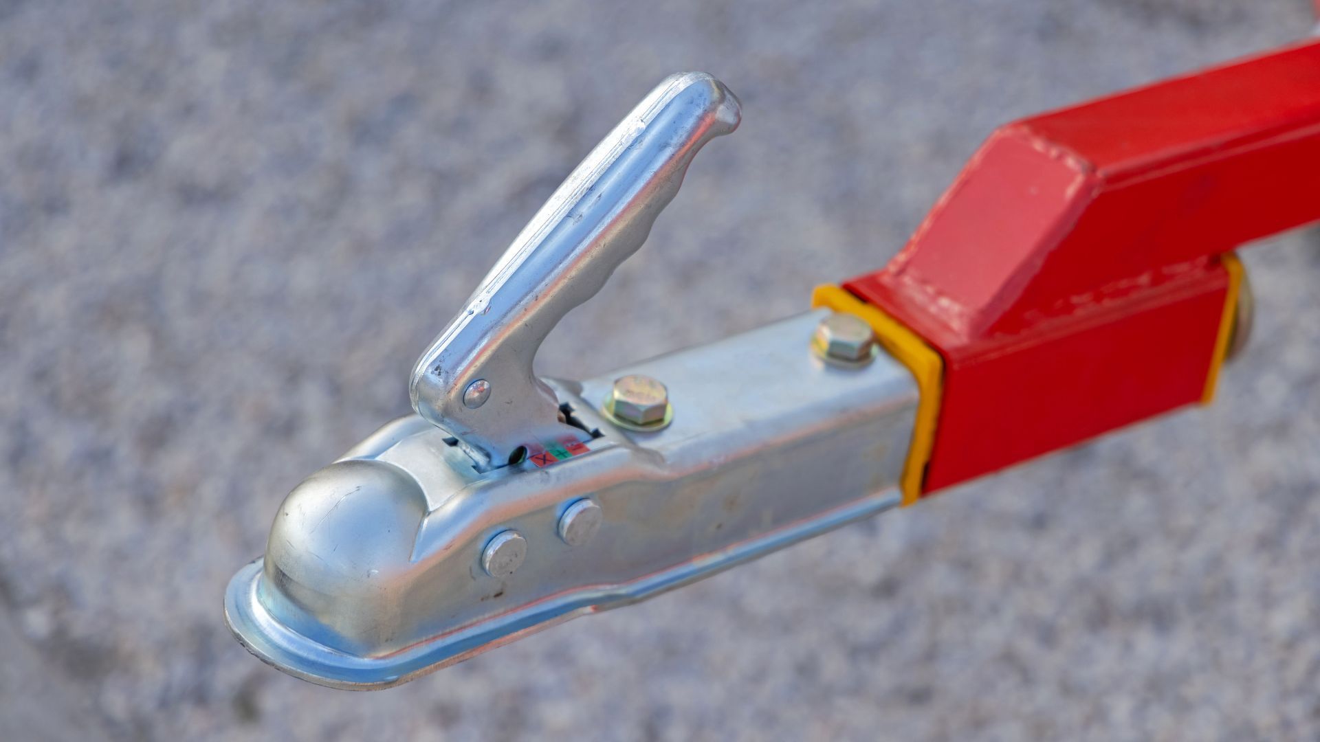 Red and silver trailer hitch on gray surface. Handle is raised.