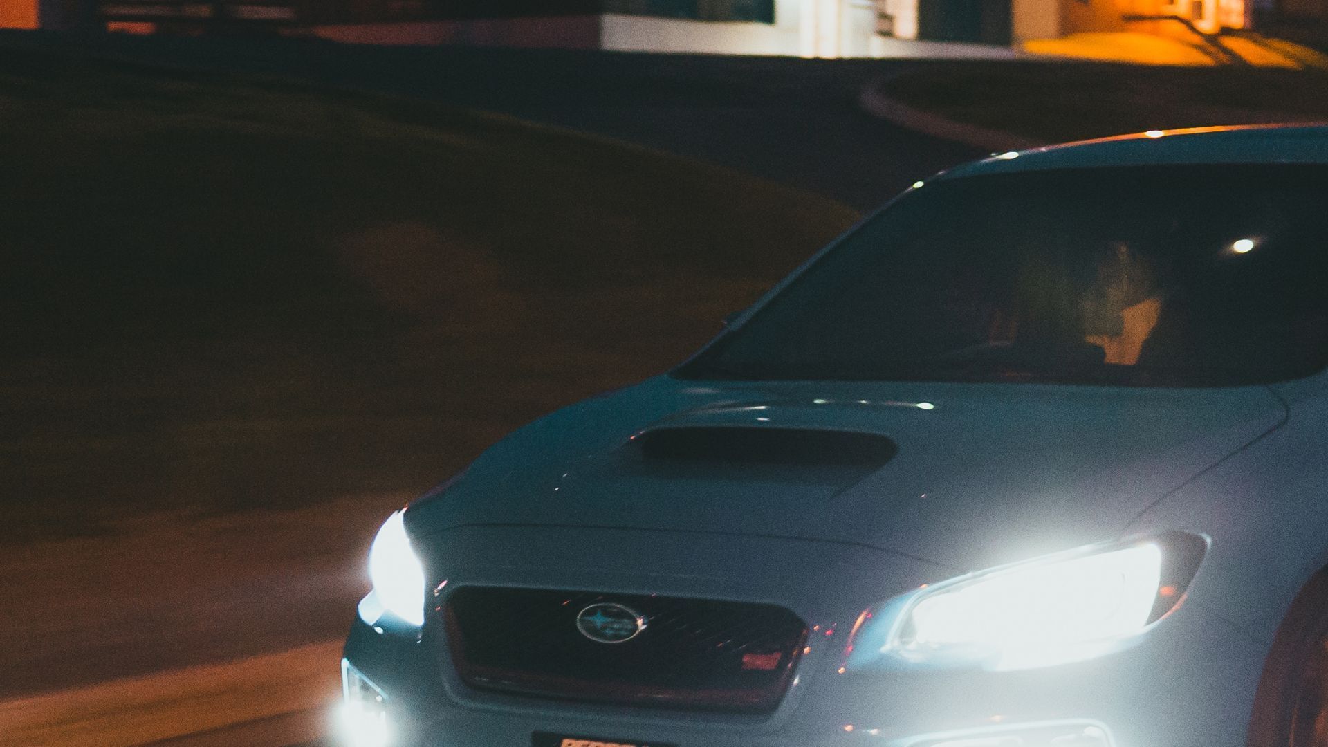 White Subaru WRX driving at night, headlights illuminated.