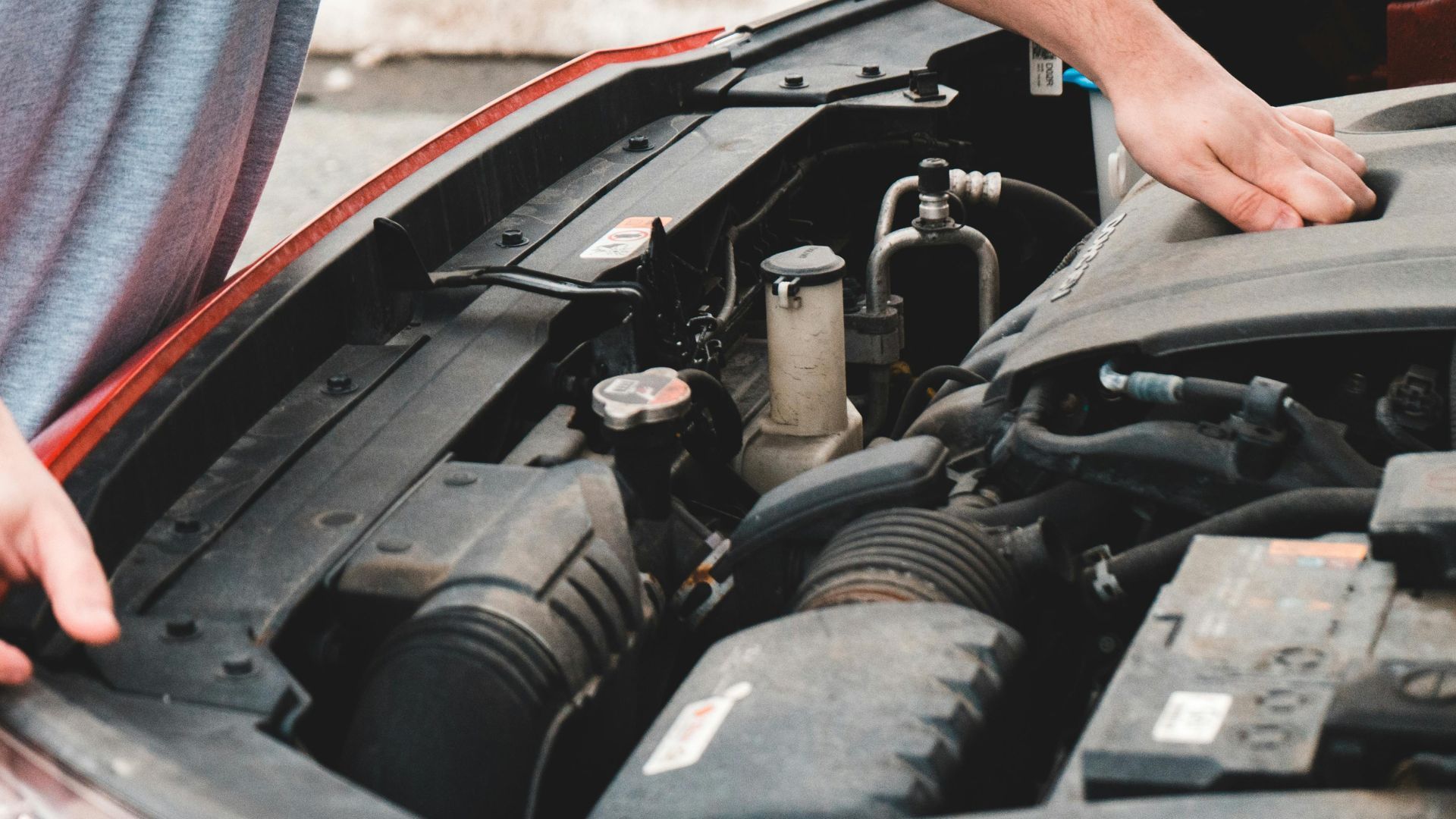 Person opening the hood of a red car, revealing the engine.