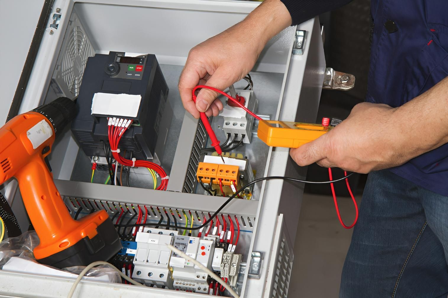 A Man is Working on an Electrical Box With a Drill and a Voltmeter — Reilly Electrical Services in Noosa, QLD