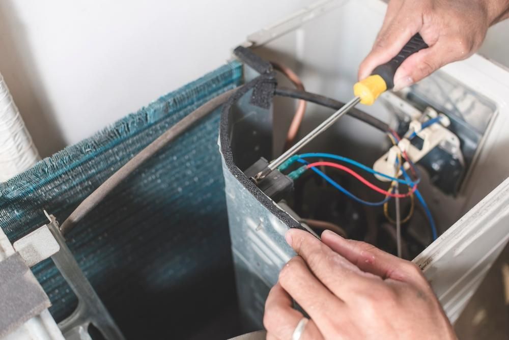 A Person is Fixing an Air Conditioner With a Screwdriver — Reilly Electrical Services in Nambour, QLD