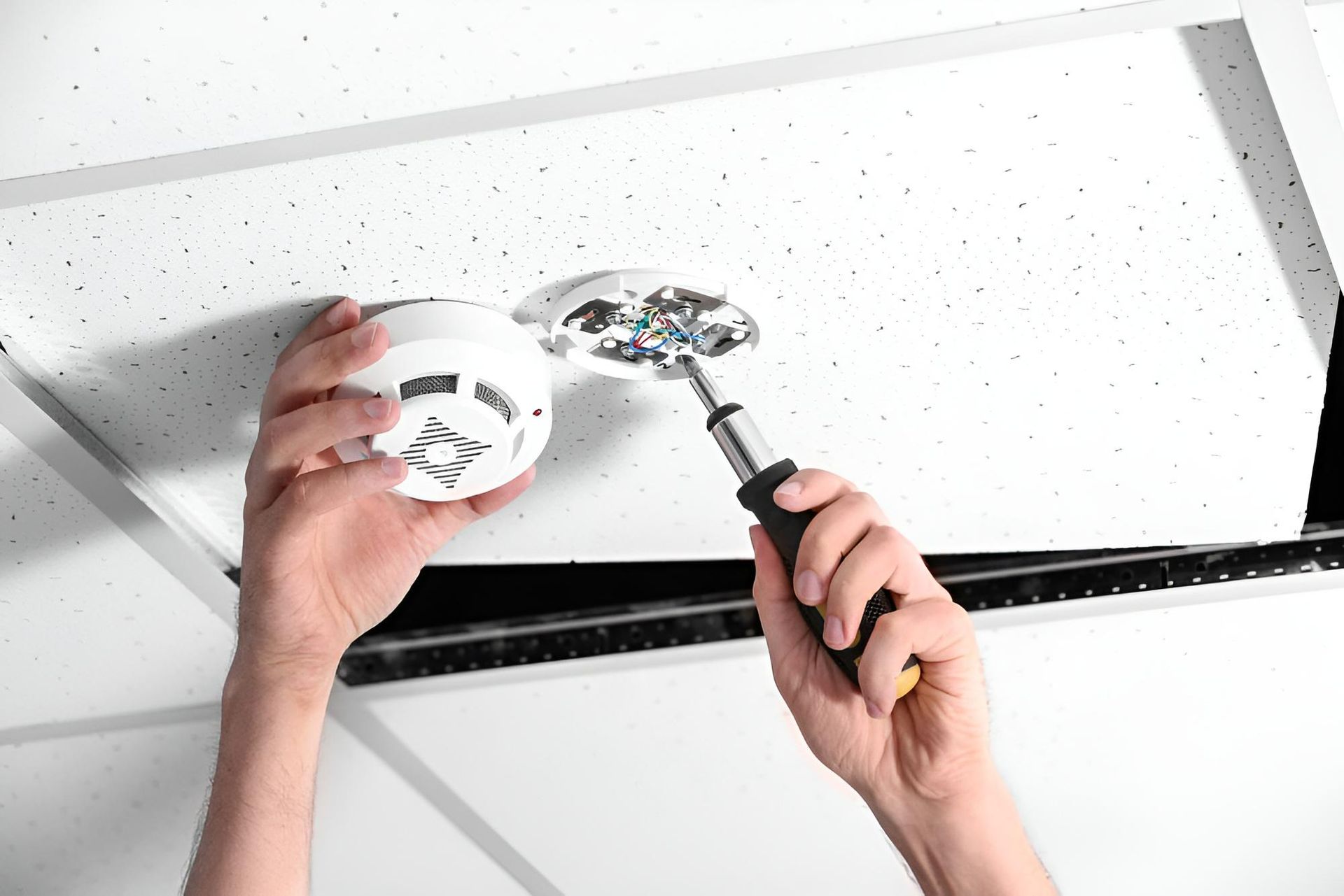 A Person is Installing a Fire Alarm on the Ceiling — Reilly Electrical Services in Noosa, QLD