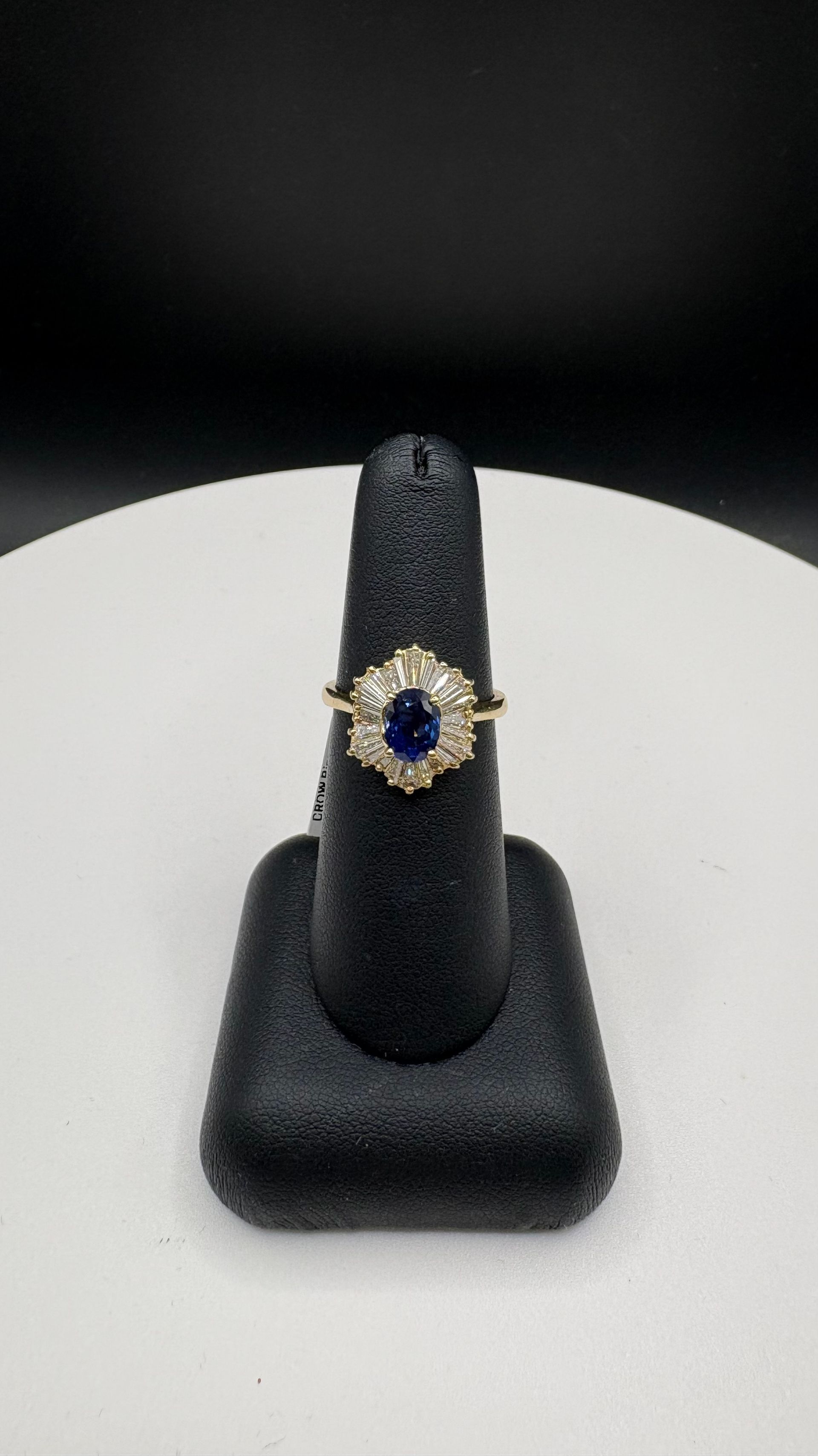 Diamond cluster ring on a white display stand against a dark background