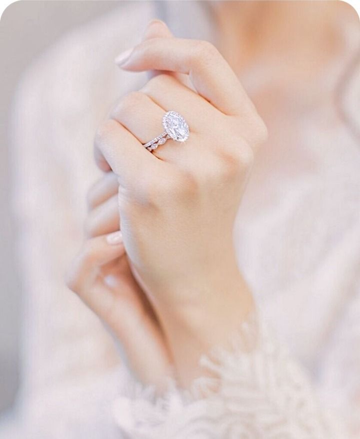 Close-up of hands wearing a sparkling diamond ring against a soft white lace background