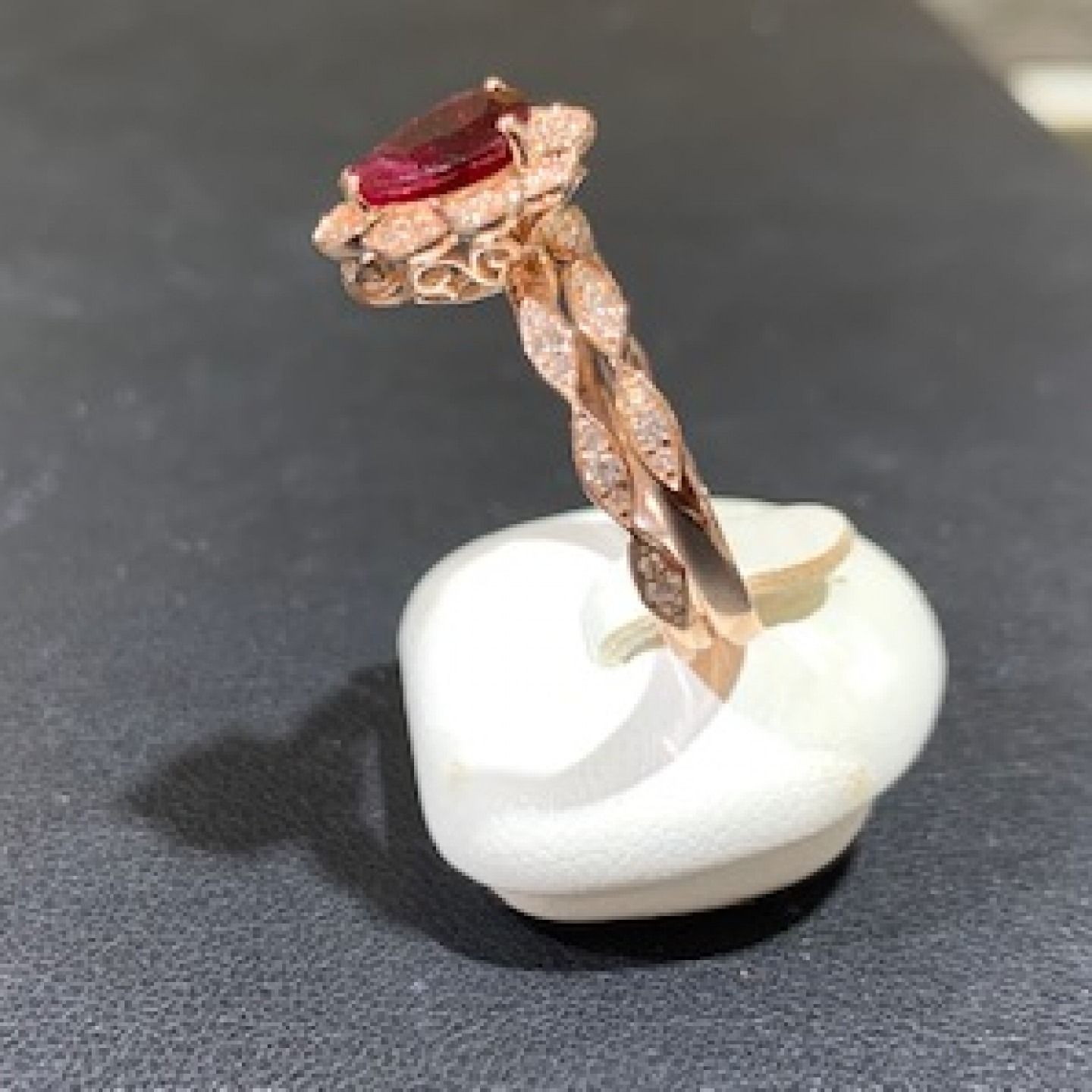 Rose gold ring with a red gemstone, displayed on a white stand against a dark background