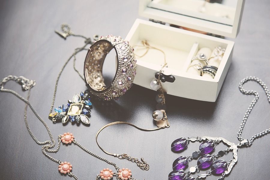 Jewelry spread on a gray surface beside an open white box, including necklaces, rings, and purple earrings