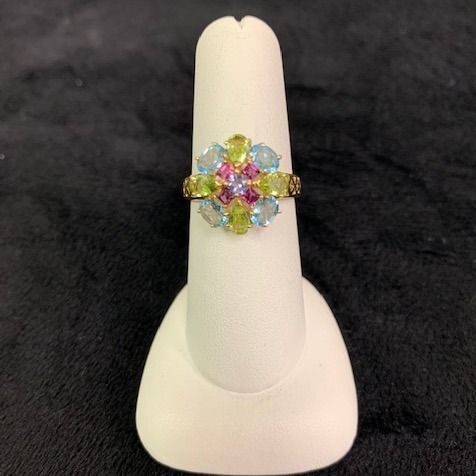 Colorful gemstone flower ring on a white display stand against a black background