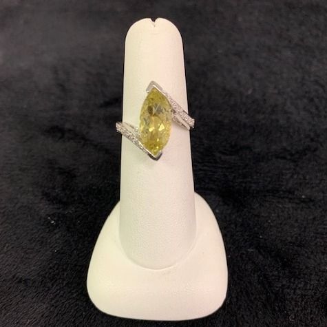 Yellow gemstone ring on a white display stand against a dark background