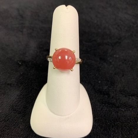 Coral cabochon ring on a white display stand against a dark background