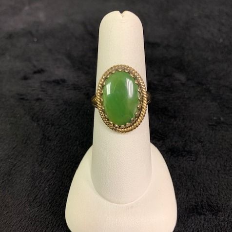 Green oval gemstone ring in a gold setting on a white display stand