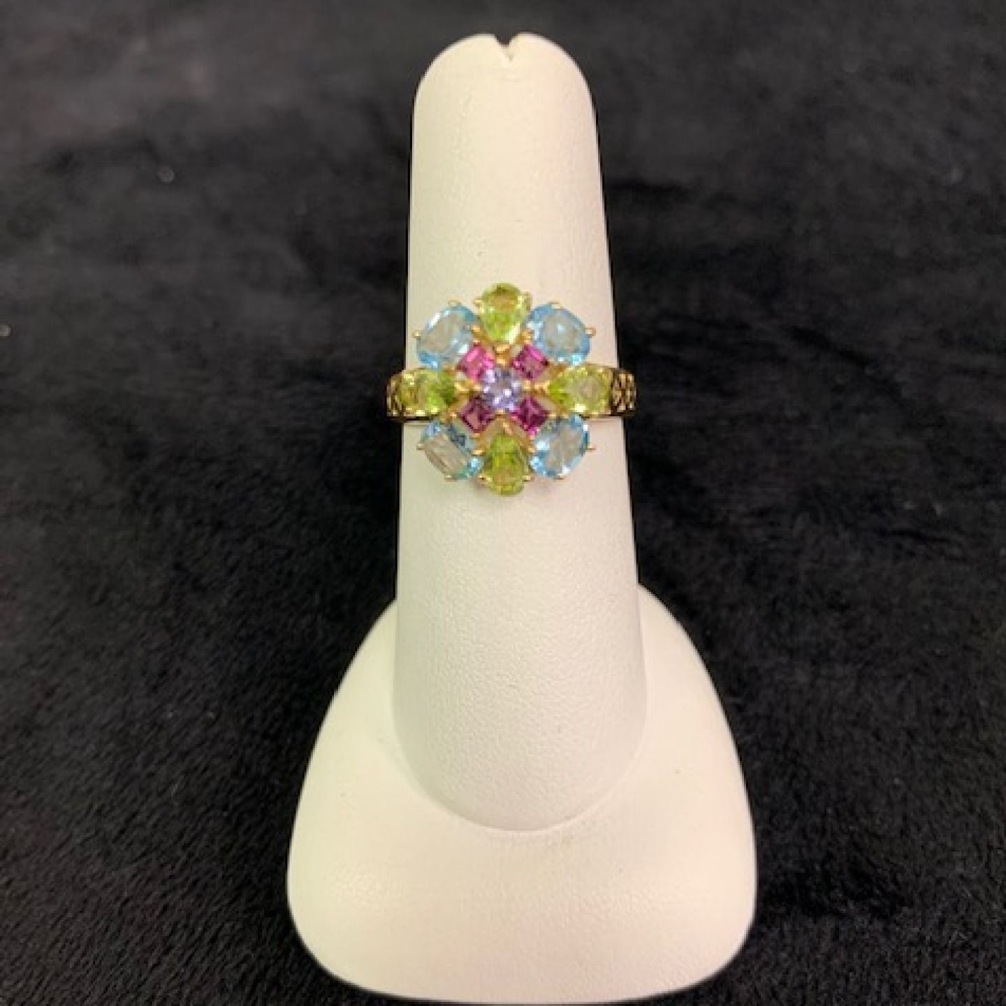 Colorful gemstone ring on a white display stand against a black background