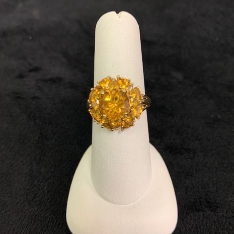 Yellow gemstone ring displayed on a white stand against a black background