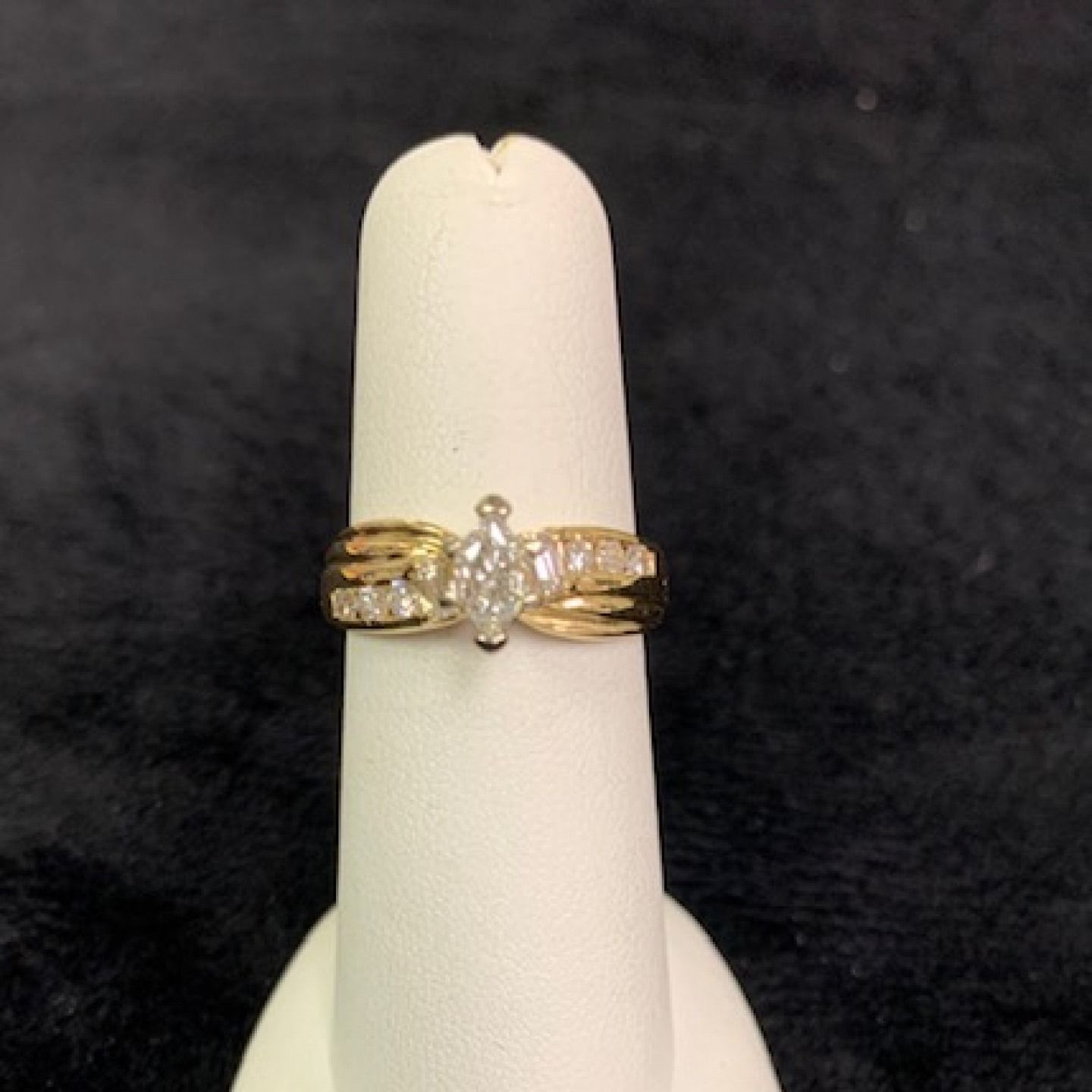 Gold ring with a central clear stone on a white display stand against a black background