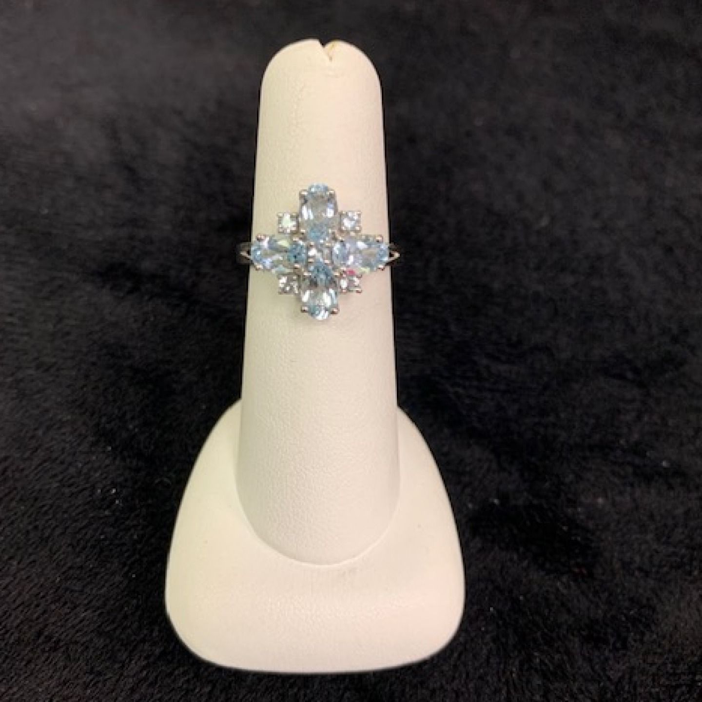 Silver snowflake ring with blue stones displayed on a white stand against a black background