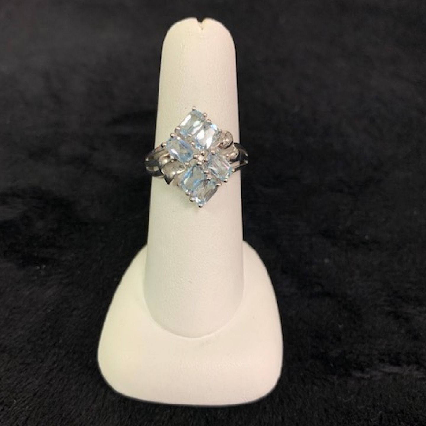 Silver ring with a square cluster of clear stones on a white display stand.