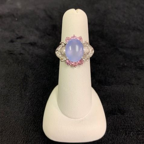 Oval blue gemstone ring with silver accents on a white display stand