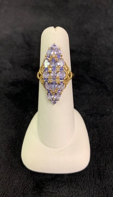 Gold ring with purple and clear gemstones on a white display stand