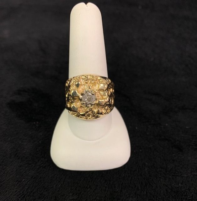 Gold ring with a large clear stone displayed on a white stand against a black background