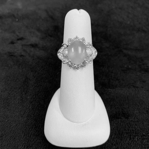 Decorative silver ring with a pale oval stone on a white display stand