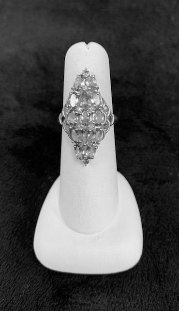 White display stand holding a silver, diamond-shaped brooch on a dark background